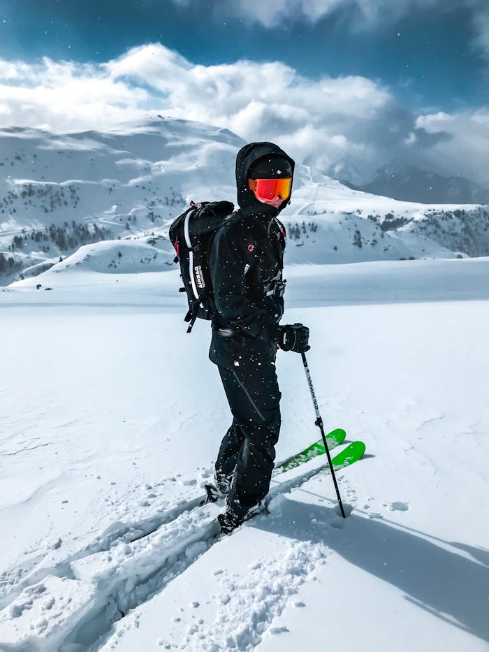 man-riding-ski-boards-2433363 A skier in black gear and goggles enjoys a sunny day on a snowy mountain landscape.